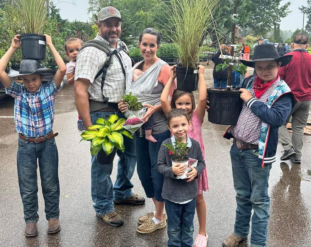 A family of eight poses with plants at the Spring Plant Sale
