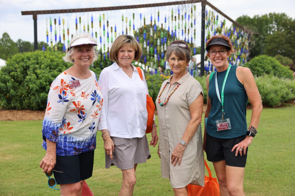 Four smiling women pose in front of a bottle wall art display