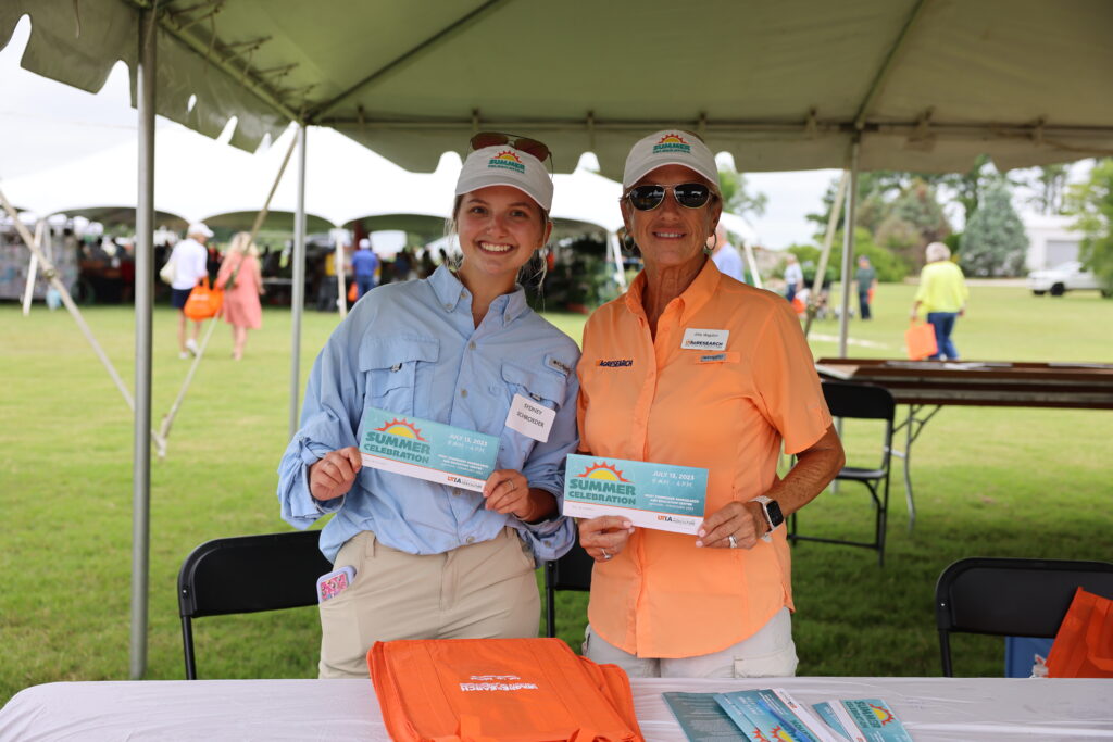 Two women pose for the camera holding an event program that says "2023 Summer Celebration"