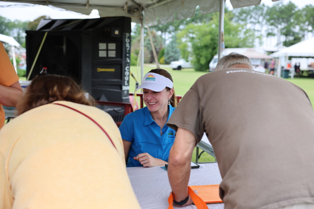 A woman smiles while helping two people at a registration booth