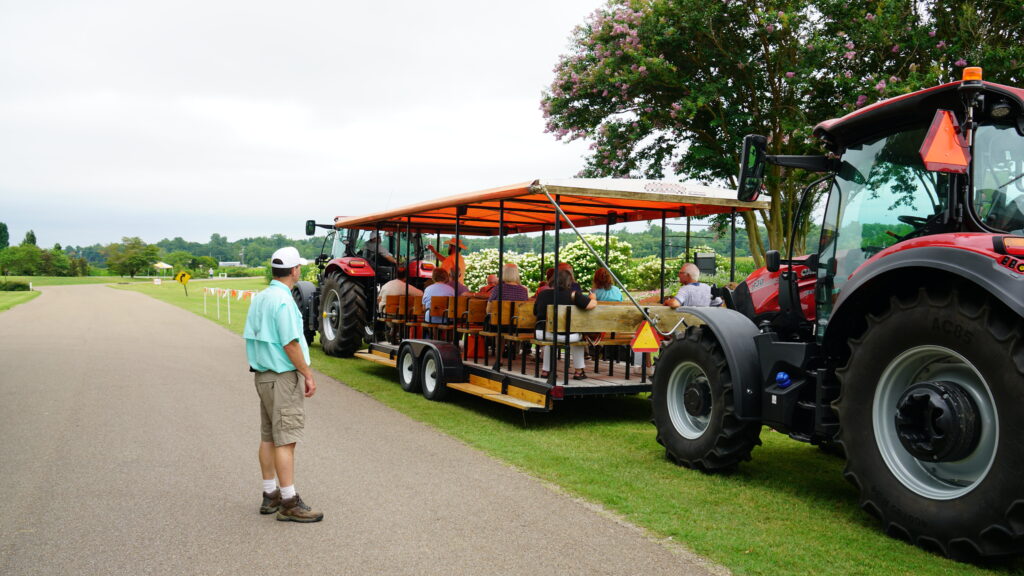 A man stands beside a tour wagon of people pulled by a tractor